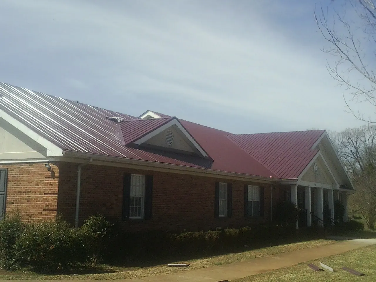 Red metal roof with gabled entries on a long brick building, from a Hail Damage Roof Repair job in Angola