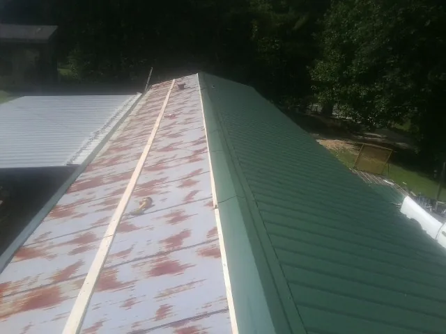 Old rusted panels beside newly installed green metal roofing — Wind Damage Roof Repair by Roofing Brothers in Angola