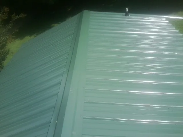 New green metal panels meeting at the ridge of a roof — Flat Roof Repair work by our crew in Angola