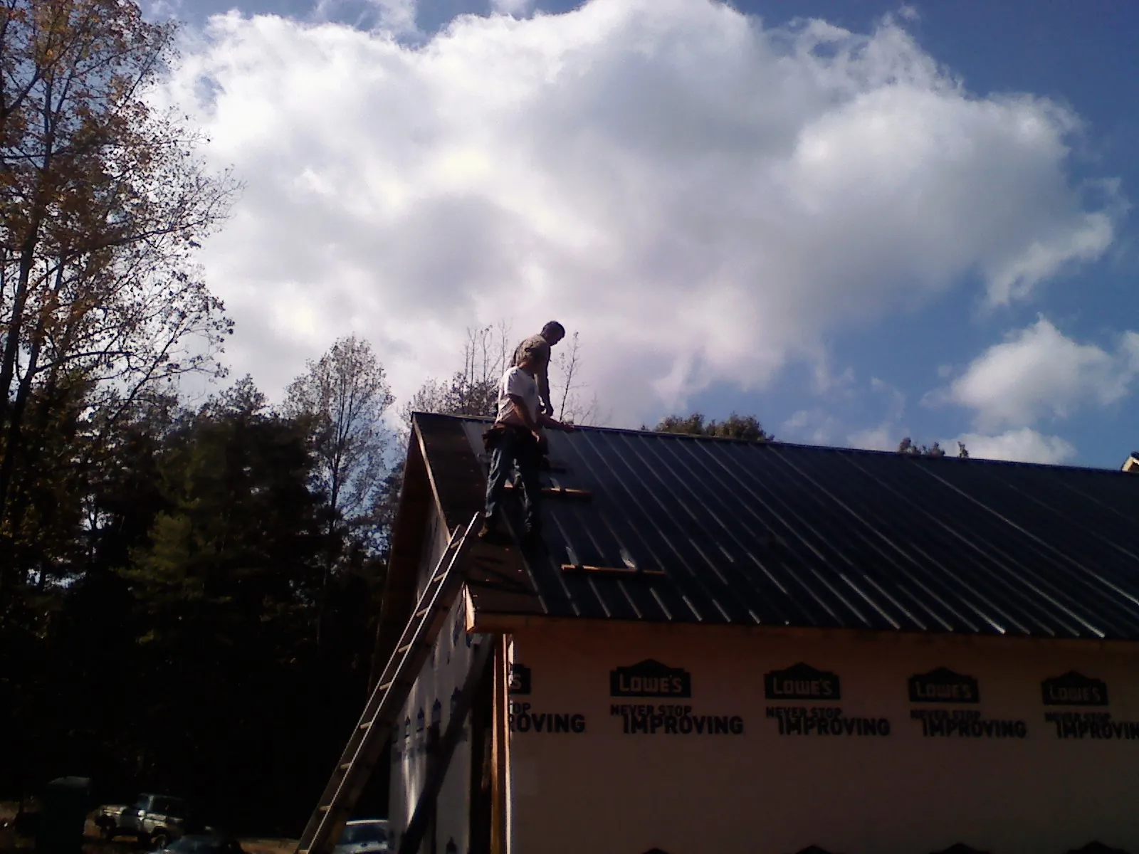 Roofer fastening dark metal panels high against a cloudy sky, from a Roof Inspection job in Angola