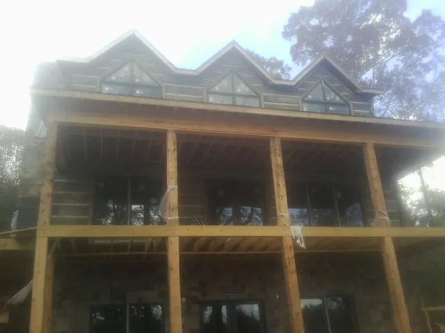 Dormers and porch framing on a large log home under construction — Roof Coating work by our crew in Angola