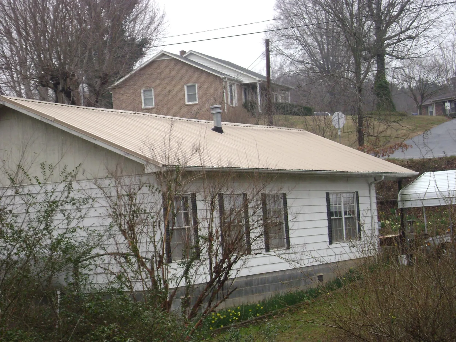 Tan metal roof on a white sided house set into a hillside — Commercial Roofing by Roofing Brothers in Angola