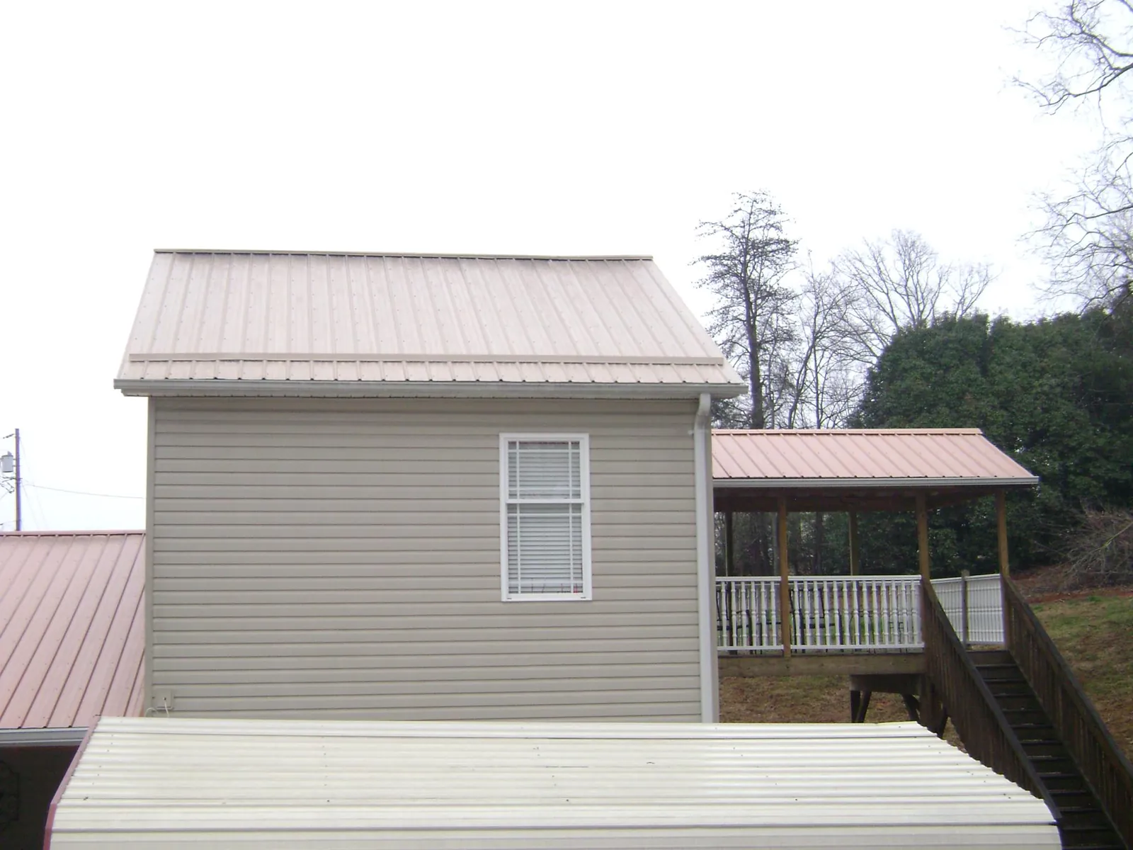 Tan metal roofs on a two story addition and attached porch, from a Roof Replacement job in Angola
